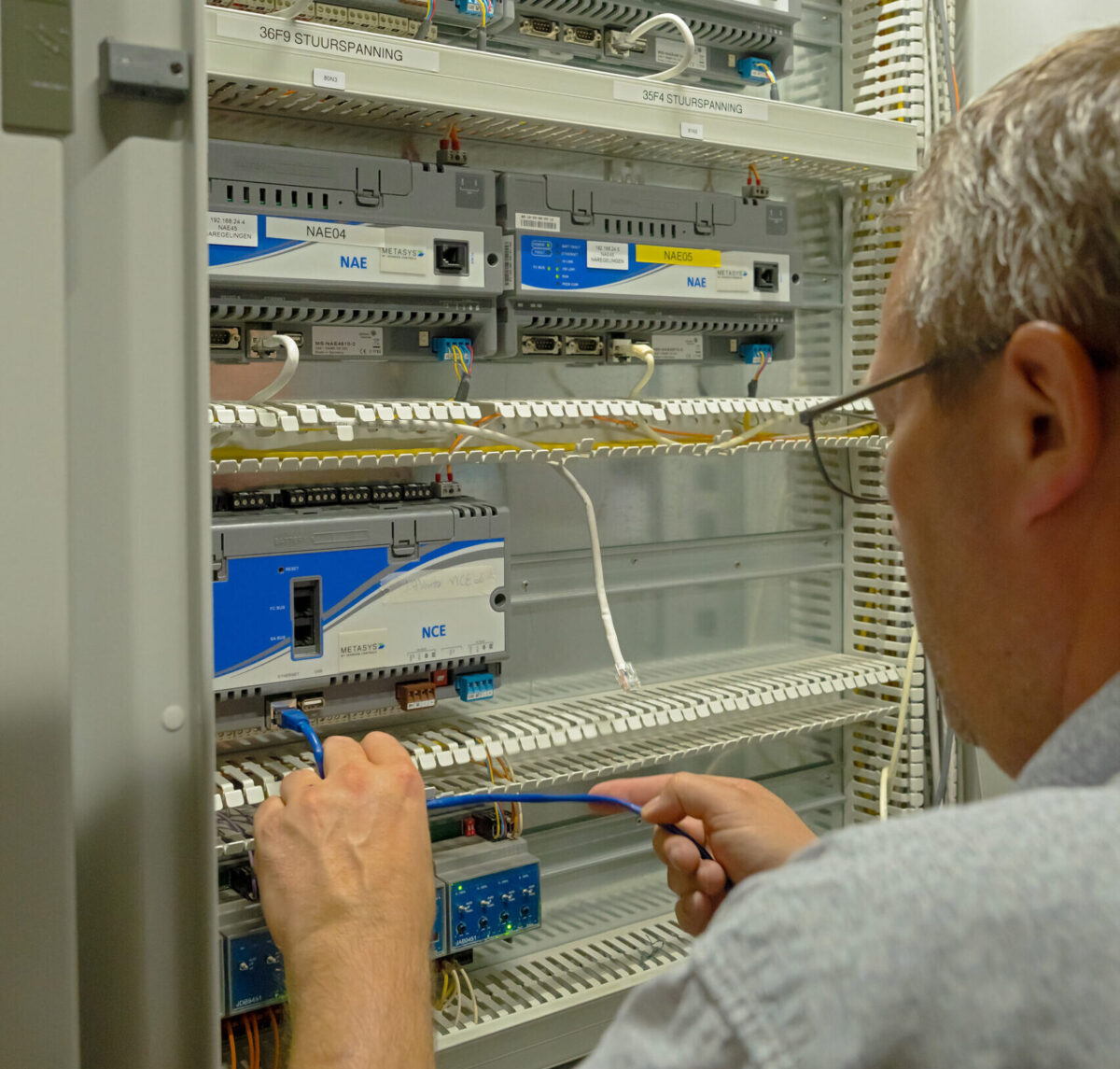 Technicus sluit netwerkkabel aan op Metasys NAE-controllers in serverkast